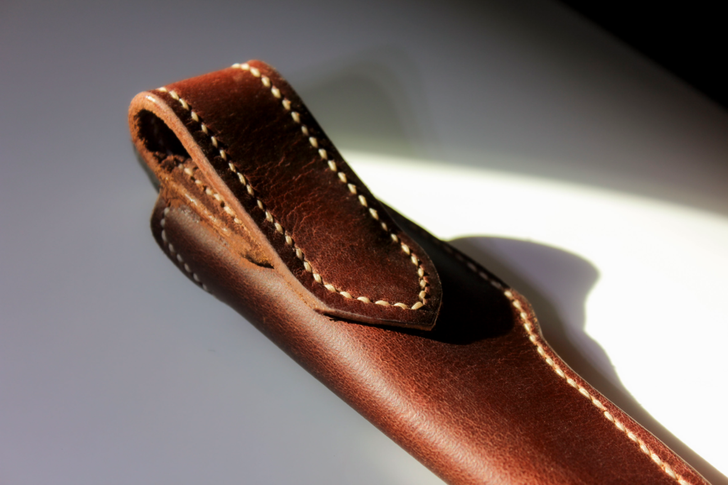 Close-up of a hand-stitched holster-style belt loop in full-grain leather, cream thread